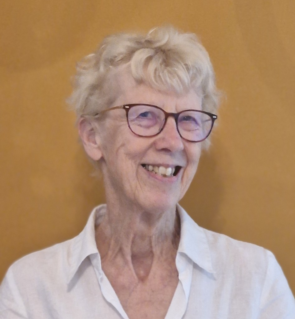Image shows head and shoulders portrait of Suzanne McConaghy also known as M. G. de Grey, smiling and  wearing a white shirt 